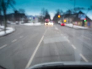 Unscharfe Sicht durch die Windschutzscheibe eines Fahrzeugs im öffentlichen Straßenverkehr bei Dämmerung.