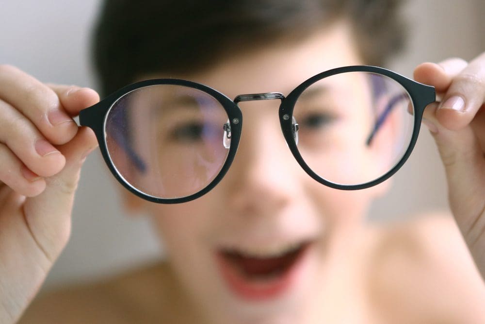 https://www.nvisioncenters.com/wp-content/uploads/young-boy-holding-glasses-in-front-of-face-1.jpg